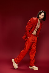 A shirtless man exudes confidence as he poses for the camera in a striking red suit, showcasing his...