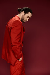 A handsome man in a red suit, without a shirt, striking a powerful pose in front of a vibrant red...