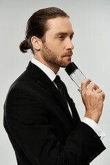 A bearded businessman in a suit passionately holds perfume bottle and posing in his sleek attire.