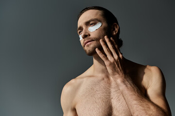Handsome, shirtless man with beard intently gazes, wearing under eye patches on his face against a...