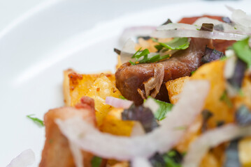 Fried meat with potatoes, onion and herbs on a white plate