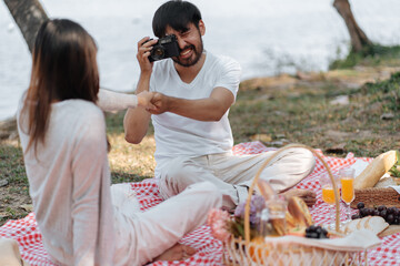 Happy asian couple travel. Man taking photo of his girlfriend picnic time in park holidays vacation