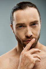 Fototapeta premium Shirtless, handsome man with beard standing in studio with finger on his nose, showing thoughtful expression.