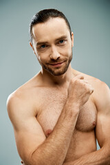 A shirtless man with a beard poses for a portrait on a grey background in a studio setting.