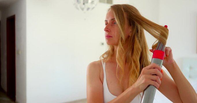 Young woman styling her long hair with a styler
