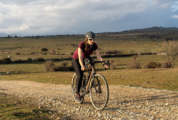 Obraz premium A woman rides a gravel bike on a picturesque rural path, surrounded by nature. Captured in natural light, the scene embodies freedom, fitness, and exploration during a countryside cycling adventure.