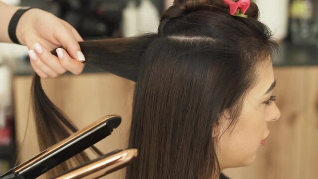 portrait of a beautiful young Caucasian woman having her hair straightened and curled with a curling iron for volume at a beauty and health salon