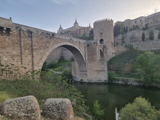 Toledo, Spain, bridge, ancient castle and towers, cathedral on the background, river and green on...