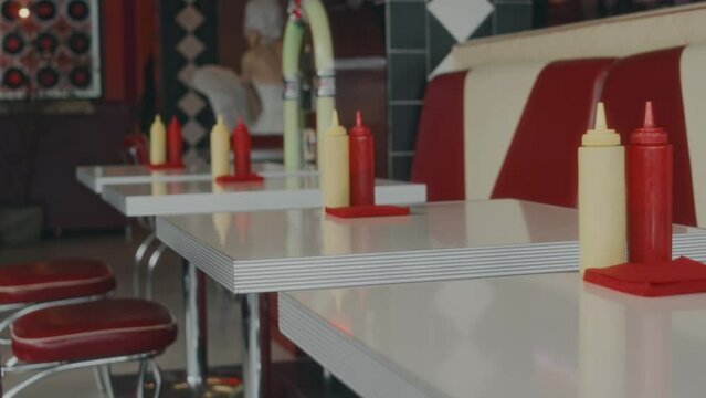 No people panning shot of row of empty tables with ketchup and mayo in 1980s style authentic American diner, design in red and white colors
