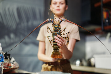 A woman holding a large lobster in a kitchen sink with water, glass of water in background