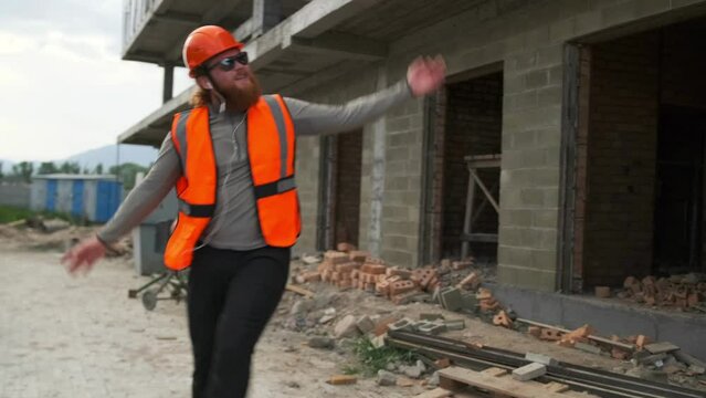Happy confident young male engineer dancing swing your arms and legs to the music while working on a construction site.