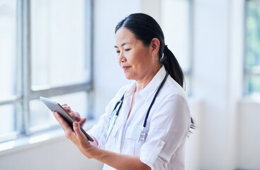Focused Female Doctor Using Digital Tablet in Bright Hospital Corridor