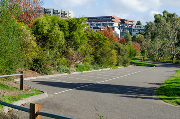 A public outdoor car park with vacant spaces in a park surrounded by lush green trees, residential...