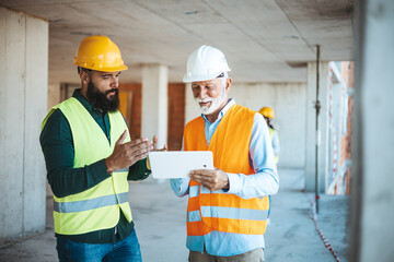 A diverse team on a construction site, with a worker and senior manager reviewing plans on a...