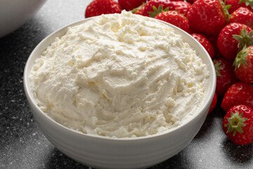 White bowl with Italian Mascarpone close up and fresh strawberries in the background 