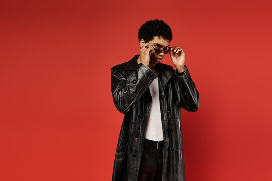 Handsome African American man posing against a striking red backdrop in a stylish black trench coat. - Powered by Adobe