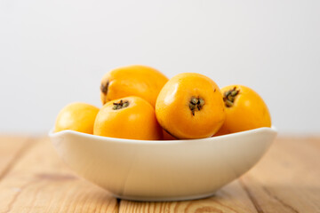 Group of loquats sitting on a bowl on a wooden table, on a light grey background