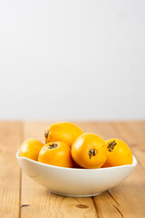 Group of loquats sitting on a bowl on a wooden table, on a light grey background