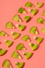Flat lay of triangle shaped kiwi slices on a pink background, lined up in a diagonal