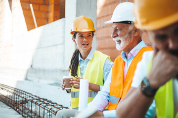 A male and female engineer in safety gear engage in a thoughtful discussion over blueprints at an active construction site, reflecting collaboration and expertise in their field.