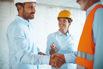 A man and a woman, both site managers wearing hard hats and safety vests, engage in a handshake,...