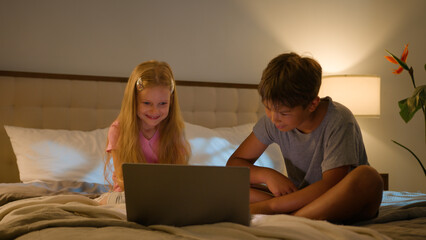 Happy family Caucasian children daughter son little kids watching movie video online Internet cartoon siblings boy girl using computer laptop bed night learning study distant education indoors bedroom