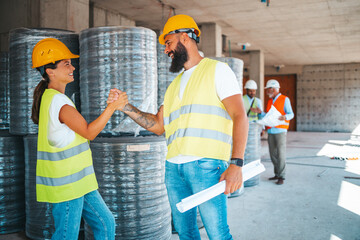 A male and female worker wearing safety vests and hard hats are engaged in a friendly handshake at...