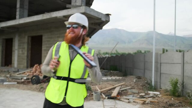 Dancing handsome construction worker moving rhythmically idle going on vacation receiving a bonus enjoying music on phone headphones with a tablet in his hands.