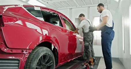 Two technicians applying red paint to a car in a specialized automotive service chamber. Quality auto body shop concept with expert car repair and painting services. Technician Inspecting Red Car