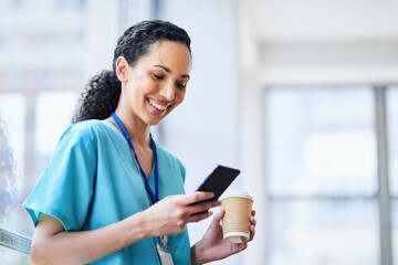 Smiling Female Doctor in Hospital Scrubs Using Smartphone with Coffee