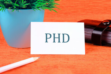 Letters PHD on a business card in a composition with a pencil, a business card holder and a plant...