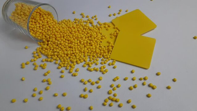 Yellow masterbatch granules spill out of the sloki, with the color chip as an example of the resulting color. This polymer is a colorant for products in the plastics industry.