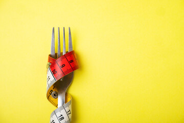 the fork is wrapped with a centimeter tape on a yellow background the concept of weight loss health