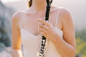 Girl musician plays the clarinet while standing in the mountains. Cropped. Faceless