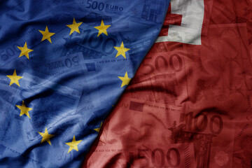 big waving realistic national colorful flag of european union and national flag of Tonga on a euro money banknotes background.
