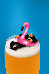 Businessman lying on floating ring in lager foamy beer glass and enjoying vacation time on blue background. Contemporary art collage. Concept of summer, vacation, relaxation, tourism