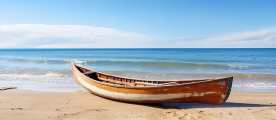 Fototapeta premium Wooden canoe resting on the sandy beach with a clear view of the ocean in the background, ideal for adding text or design in the copy space image.