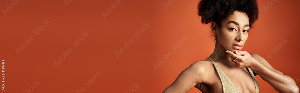 Sticker Young African American woman striking a pose in trendy swimsuit against vibrant orange backdrop.