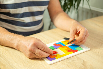 male hand manipulates colorful wooden puzzle, elderly old man composing geometric shapes, brain...