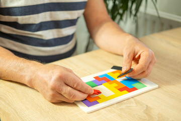 Obraz premium male hand manipulates colorful wooden puzzle, elderly old man composing geometric shapes, brain health and mental well-being, preventing dementia and Alzheimer's disease