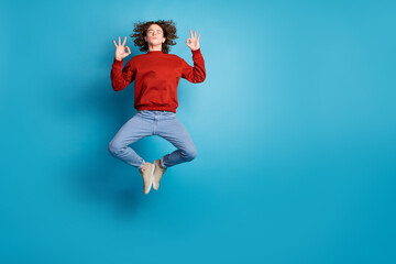 Full length photo of attractive funny guy wear red sweater jumping high showing okey signs emtpy...