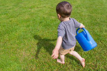 The boy watering vegetable garden from a watering can near a greenhouse