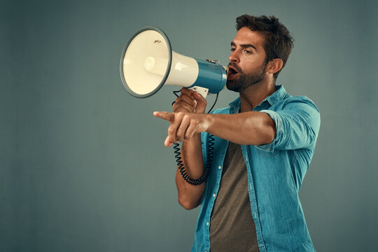 Voice, megaphone and man in studio for change, human rights or demonstration on gray background. Protest, politics and male person pointing for government reform, accountability or call to action