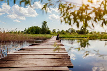 Military man fishing sitting on bridge across river holding rod throwing bait into water. Mental...