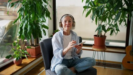Older woman with headphones on head, listening music, relaxing at home.