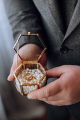 A man is holding a small box with two rings inside. The box is made of glass and has a gold frame....
