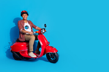 Full length photo of good mood guy wear stylish t-shirt helmet ride on moped near empty space offer isolated on blue color background