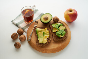 A close-up of a breakfast meal consisting of two slices of avocado toast, a cup of tea, a red...