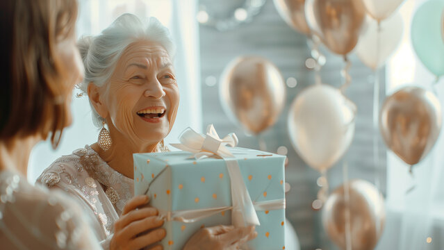 Senior woman with gray hair, wearing an elegant outfit, joyfully opening a birthday gift, surrounded by family, bright sunny room with balloons