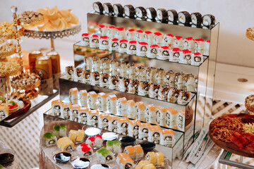 A display of sushi with a variety of colors and shapes. The sushi is arranged on a metal stand, and there are several bowls and plates of food around it. Scene is appetizing and inviting